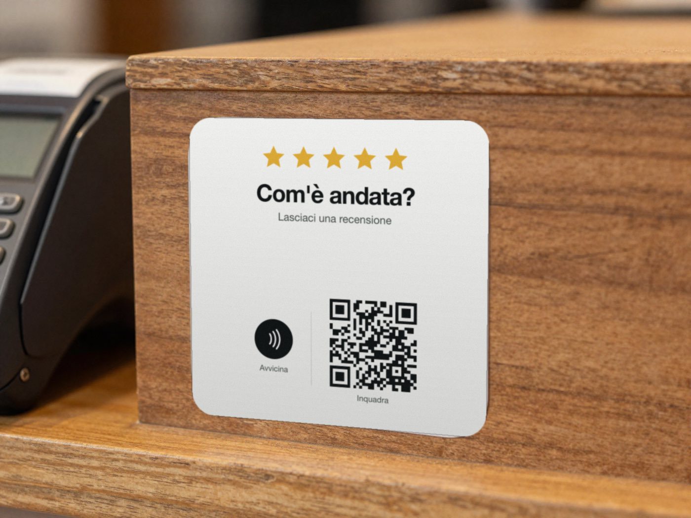 Un adesivo quadrato bianco sul fianco del bancone, accanto al POS: cinque stelle, Com’è andata?, il simbolo NFC e il codice QR.