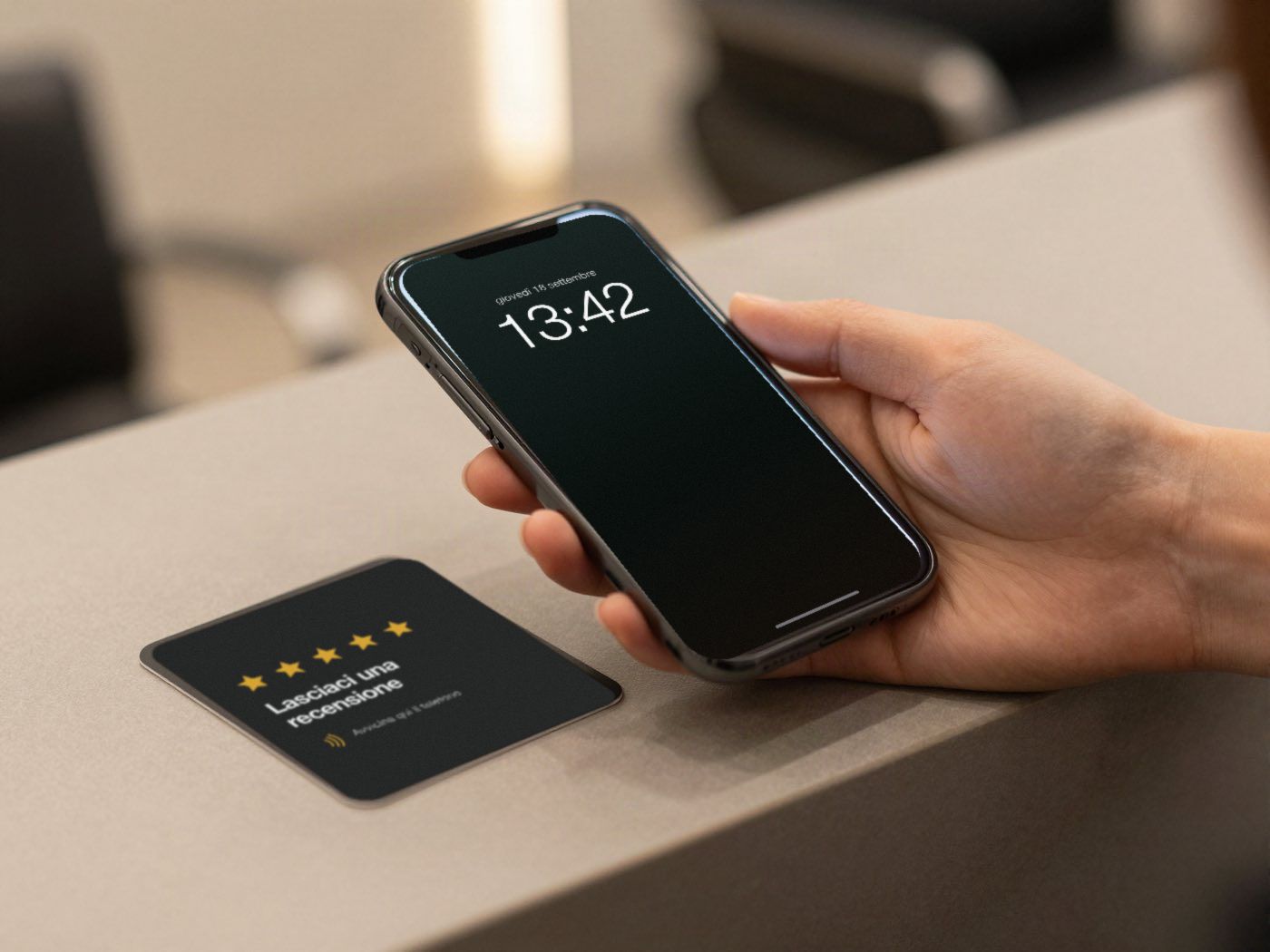 Una card scura con le stelle sul bancone e una mano che tiene il telefono: sullo schermo si apre la finestra per lasciare una recensione.