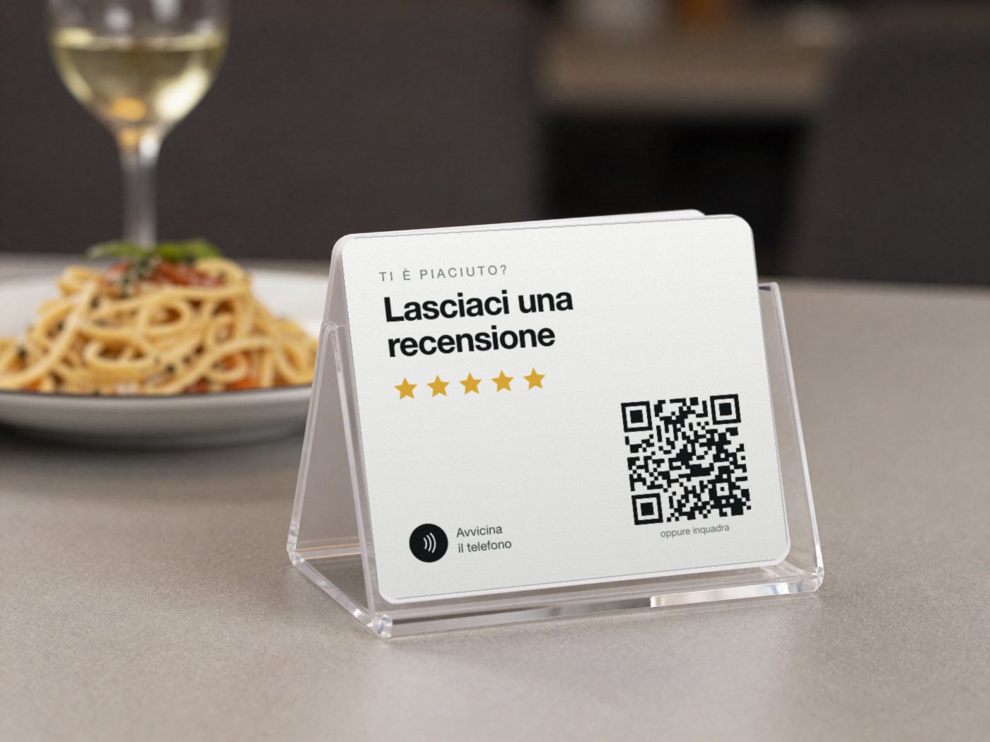 Un espositore trasparente sul tavolo di un ristorante con il cartoncino: Lasciaci una recensione, cinque stelle, il simbolo NFC e il codice QR.